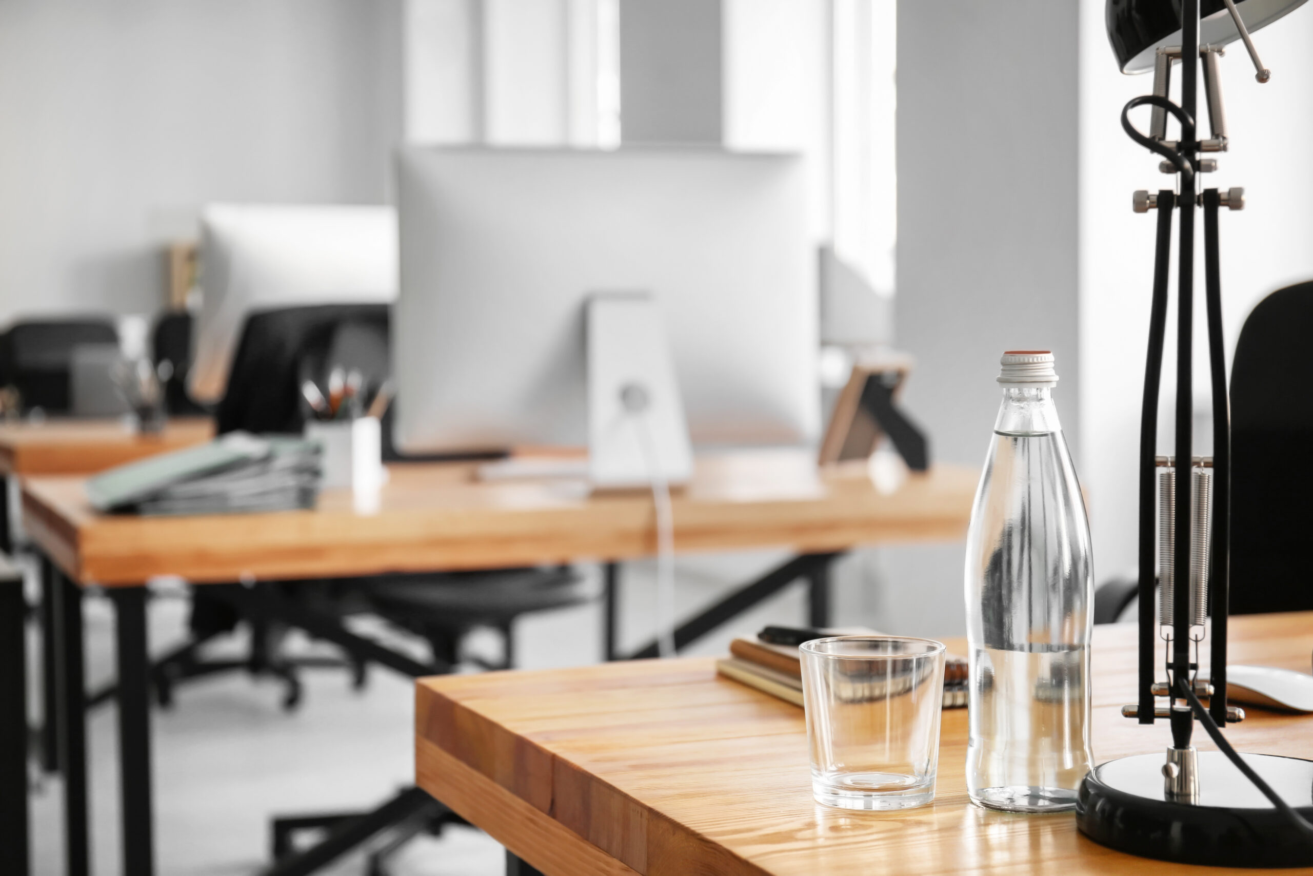 Workplace with bottle of water, lamp and notebook on table in modern office